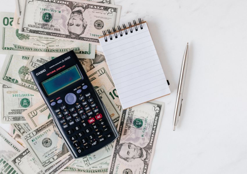 calculator and note pad on top of a bunch of American dollar bills